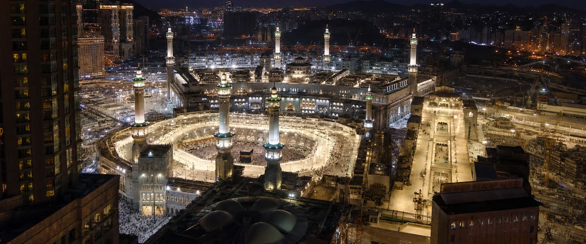Night view of Masjid al-Haram and the Kaaba glowing below a high hotel floor in Makkah