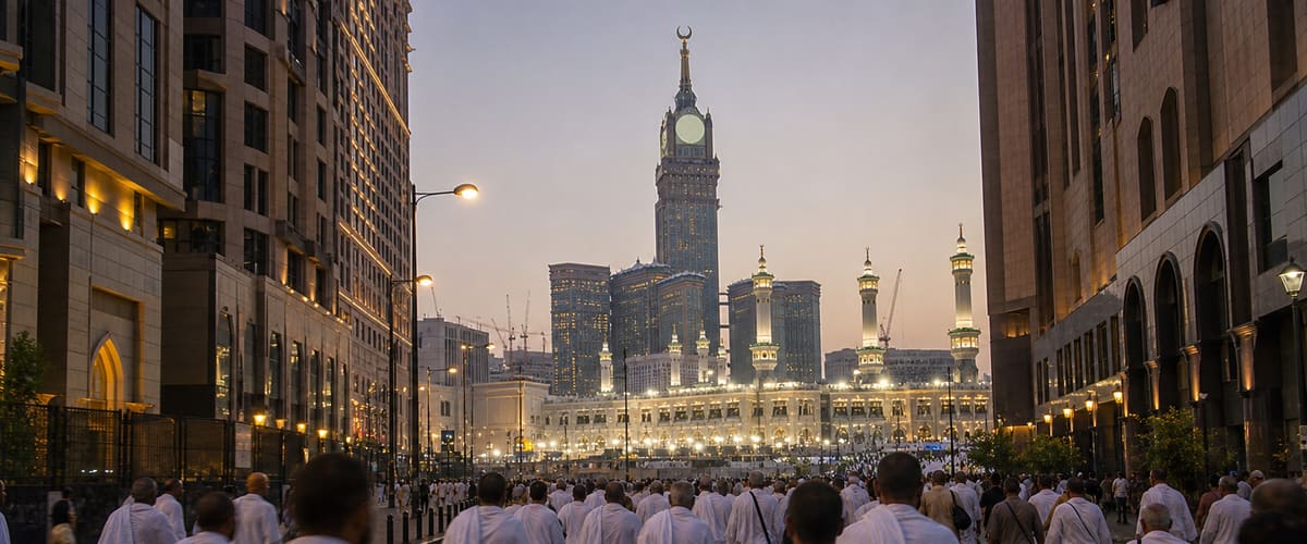 Pilgrims in white ihram walking along a Makkah street towards Masjid al-Haram and the Clock Tower at dusk