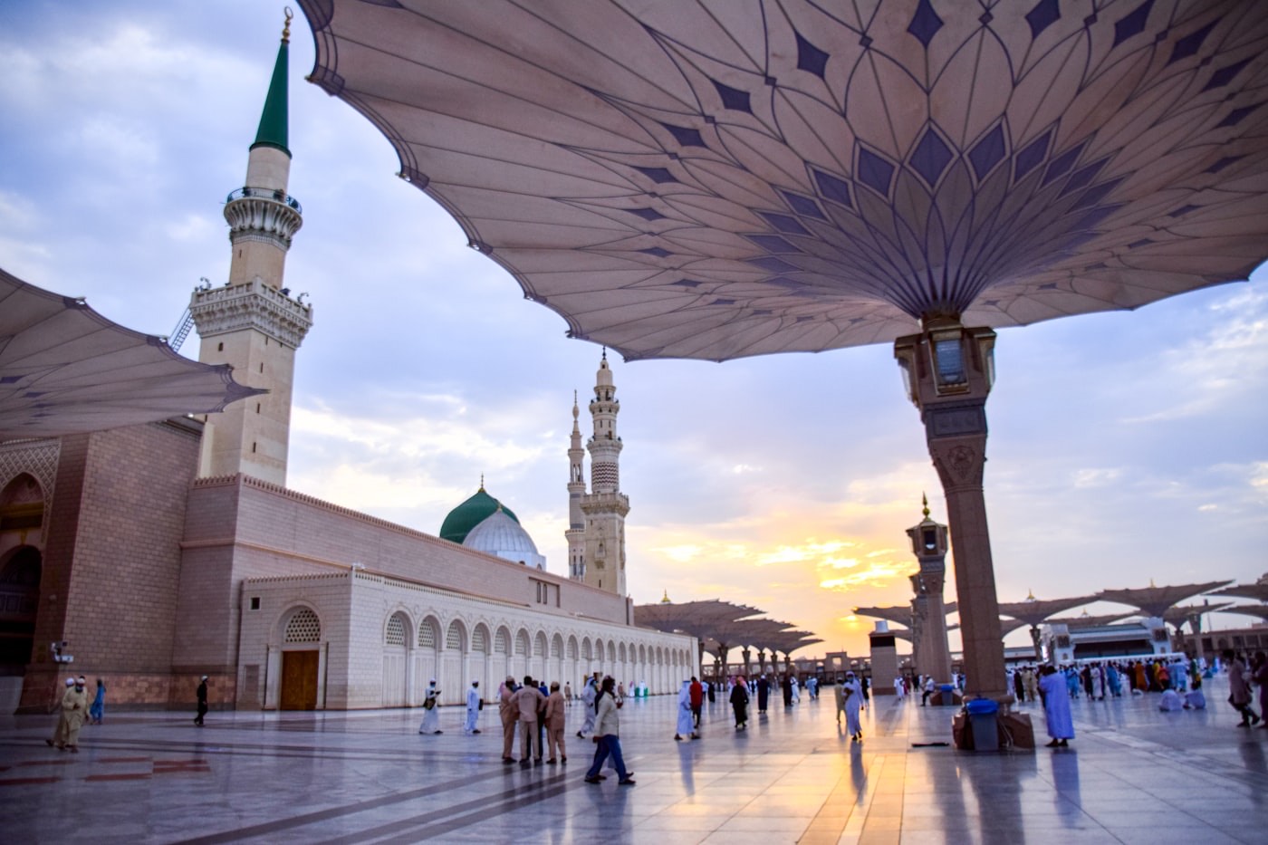 Pilgrims walking across the white marble courtyard of Masjid an-Nabawi under the giant umbrellas